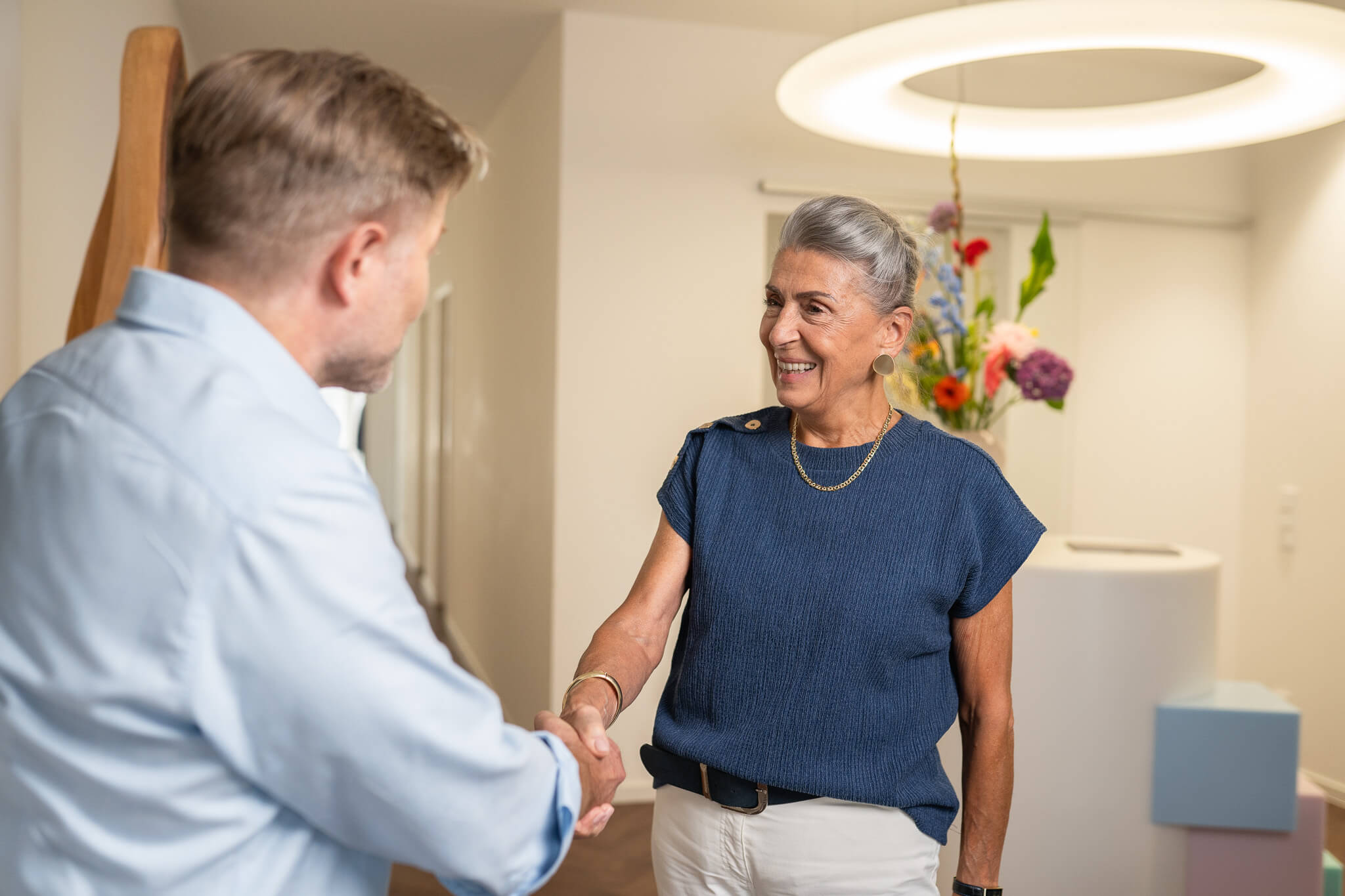 Freundlicher Empfang in der DD – Praxis für Zahnheilkunde Oberursel: Ältere Patientin wird mit einem Lächeln per Handschlag begrüßt