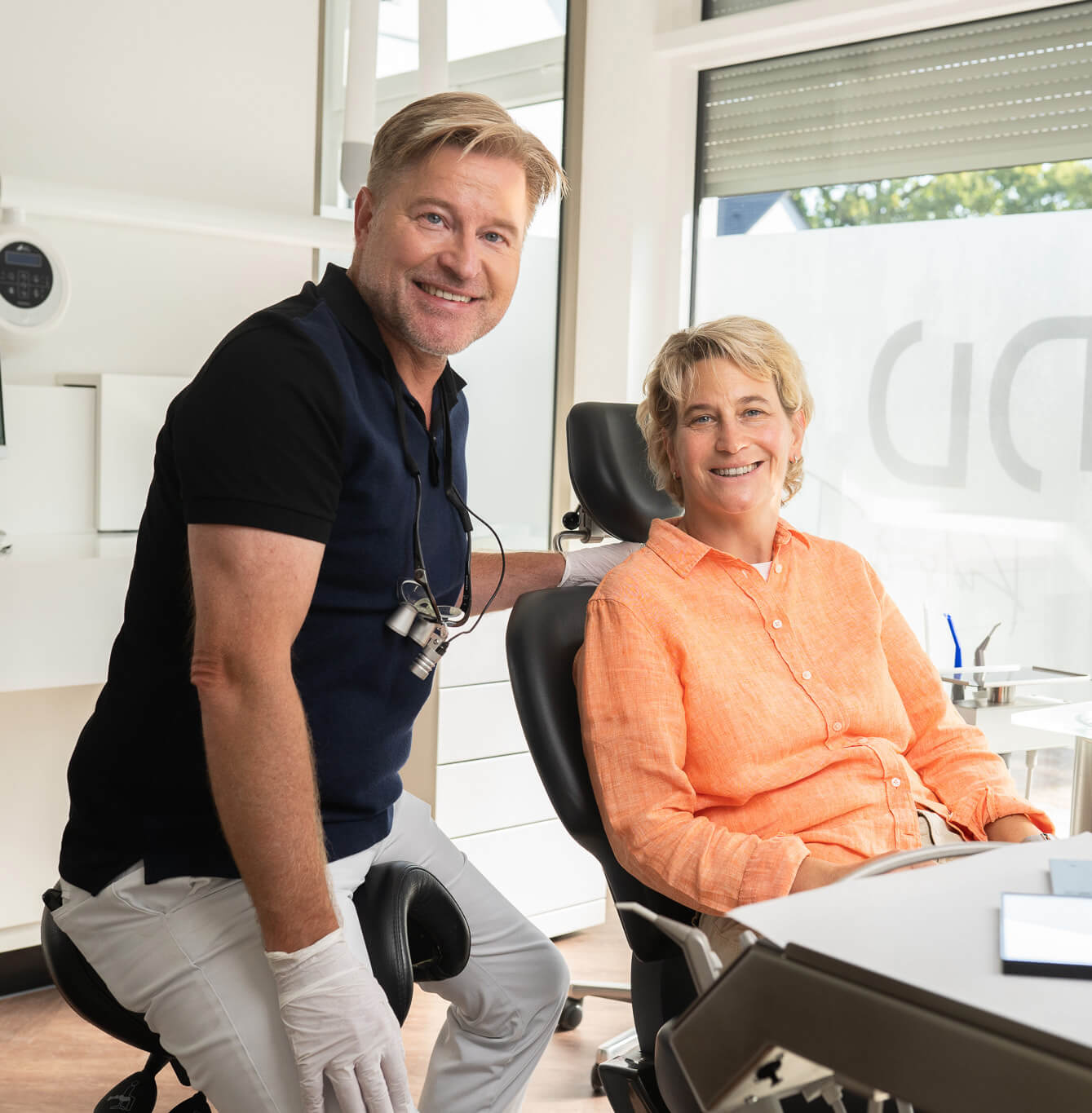 Dr. Dettler von der DD – Praxis für Zahnheilkunde Oberursel gemeinsam mit einer lächelnden Patientin im Behandlungsstuhl, beide blicken freundlich in die Kamera